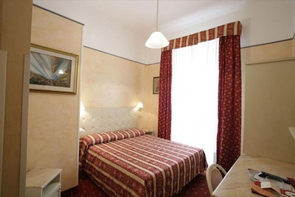 Elegantní ložnice s velkou postelí a červenými závěsy.  