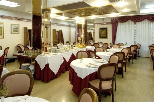 Elegantní restaurace s kulatými stoly pokrytými bílými ubrusy a hnědými židlemi.