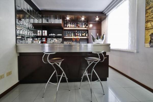 Moderní bar s židlemi u pultu a plným regálem lahví vzadu.  