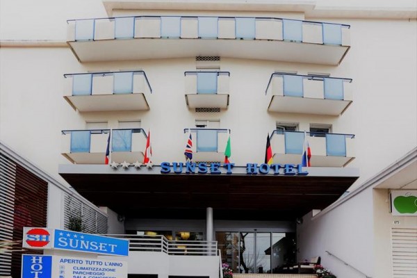 Budova hotelu Sunset se skleněnými balkony a vstupem, kde visí několik vlajek.