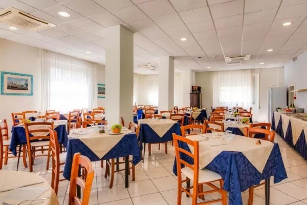 Světlá jídelna s dřevěnými židlemi a modro-bílými ubrusy na stolech.