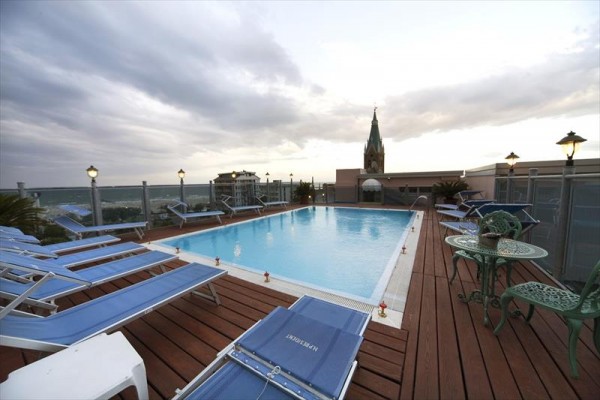 Střešní terasa hotelu s bazénem, lehátky a výhledem na město.