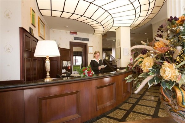 Recepce hotelu s pracovnicí za pultem, vedle květinové dekorace.
