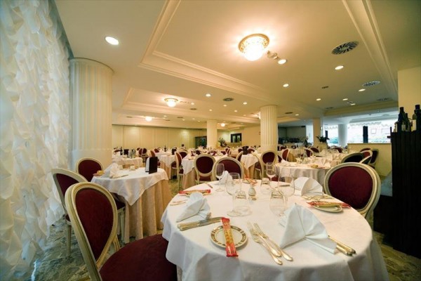 Elegantní restaurace s kulatými stoly pokrytými bílými ubrusy a složenými ubrousky.