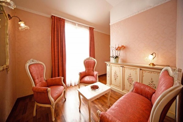 Elegantní obývací pokoj s růžovými křesly a pohovkou, bílým stolem a ozdobnou komodou s lampou a květinou.