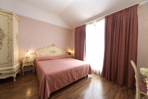 Ložnice s růžovými závěsy, zdobným nábytkem a dřevěnou podlahou.