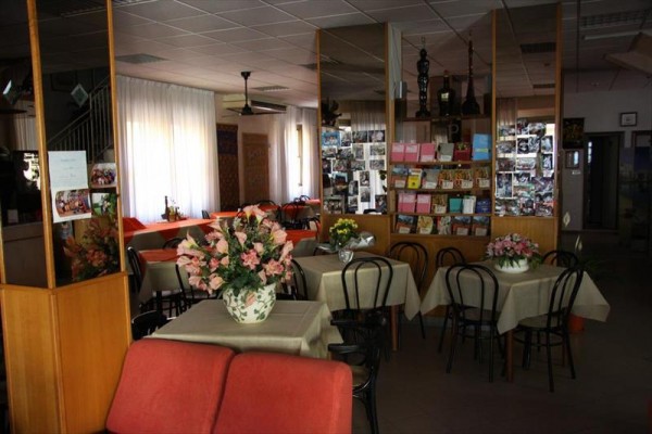 Restaurace s květinami na stolech a stojanem s pohlednicemi.