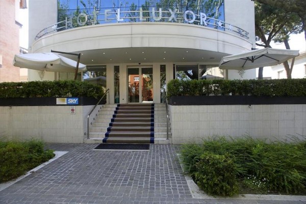 Vchod do moderního hotelu s terasou a slunečníky.