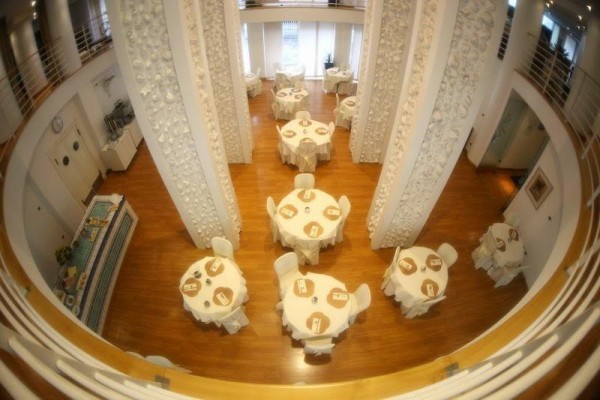 Pohled ze shora na elegantně prostřenou restauraci s kulatými stoly a zdobenými pilíři.