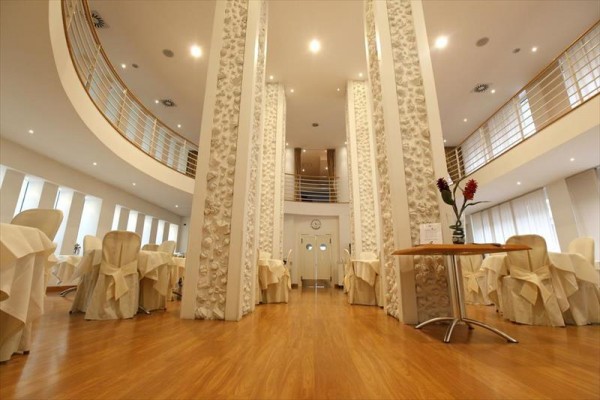 Světlá restaurace s kulatými stoly a bílými židlemi, dekorovaná rostlinami.  