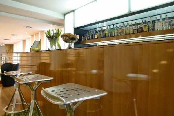 Moderní bar s dřevěným pultem, květinami a lahvemi alkoholu.