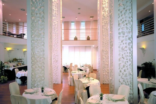 Restaurace s bílými kulatými stoly a ozdobnými sloupy.