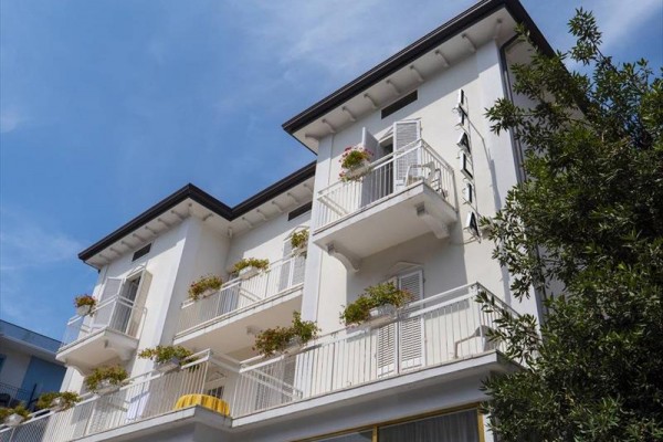 Bílá třípatrová budova s balkony zdobenými květinami.