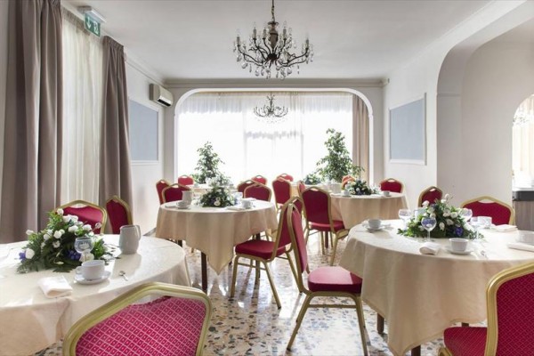 Elegantní banketová místnost s kulatými stoly, červenými židlemi a květinovými aranžmá.