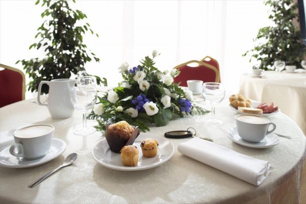 Elegantně prostřený stůl s kávou, muffiny a květinovou dekorací.