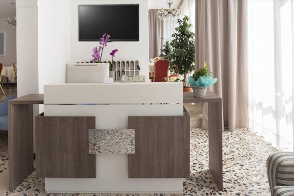 Moderní hotelová recepce s dekoračními rostlinami a obrazovkou na zdi.