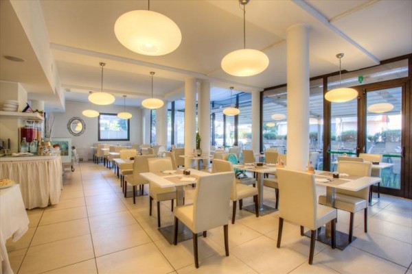 Světlá moderní restaurace s bílými stoly a židlemi.