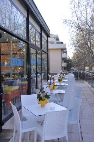 Terasa restaurace s bílými stoly a židlemi, ozdobená květinami.