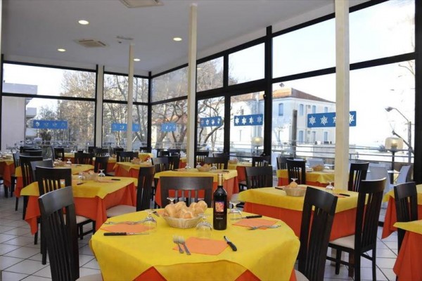 Restaurace s prosklenými stěnami, stoly s žlutými ubrusy a připravenými příbory.