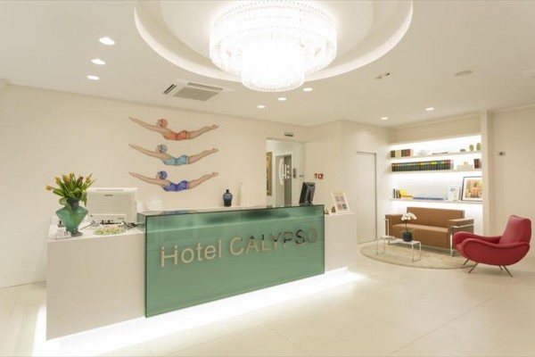 Recepce hotelu Calypso s moderním designem, obrazy plavců na stěně a skleněným lustrem.