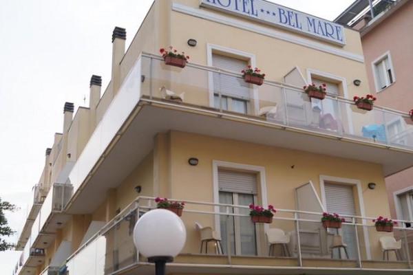Třípatrová budova hotelu Bel Mare s balkonem zdobeným květinami.  