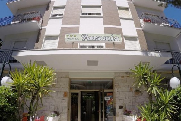 Vstup do třípatrového hotelu se zelenými rostlinami kolem.