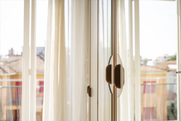 Skleněné dveře s dřevěným madlem otevřené na balkon s bílými závěsy.