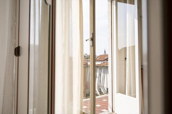 Otevřené balkónové dveře s výhledem na střechy města.