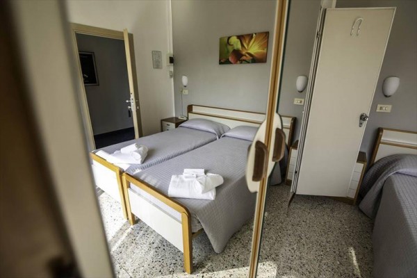 Dva jednolůžka s šedými přehozy a složenými ručníky na postelích v hotelovém pokoji.  