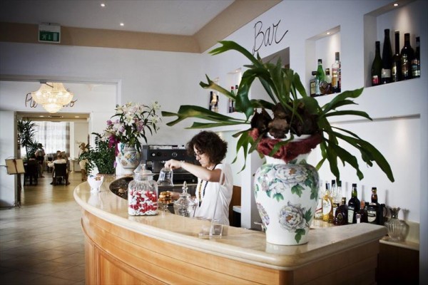 Žena za barem připravuje nápoje v elegantní restauraci s květinovou dekorací.