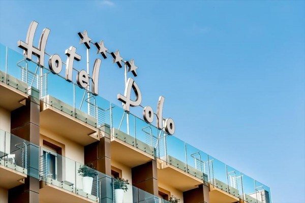 Budova hotelu Polo se čtyřmi hvězdičkami a skleněným zábradlím na balkonech.