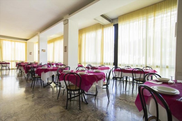 Restaurace s růžovými ubrusy a skleněnými tabulemi u oken.