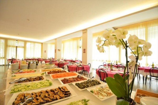 Restaurace s velkými okny, bufetovým stolem plným jídla a orchidejí v popředí.