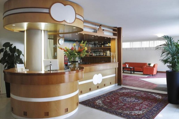 Lobby s kulatým recepčním pultem, květinami a červeným kobercem.