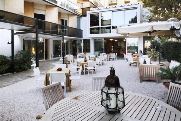 Venkovní terasa restaurace s dřevěným nábytkem a stoly s ubrusy.
