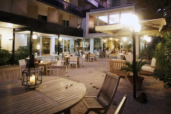 Venkovní posezení s dřevěnými stoly a židlemi v osvětlené zahradní terase restaurace.