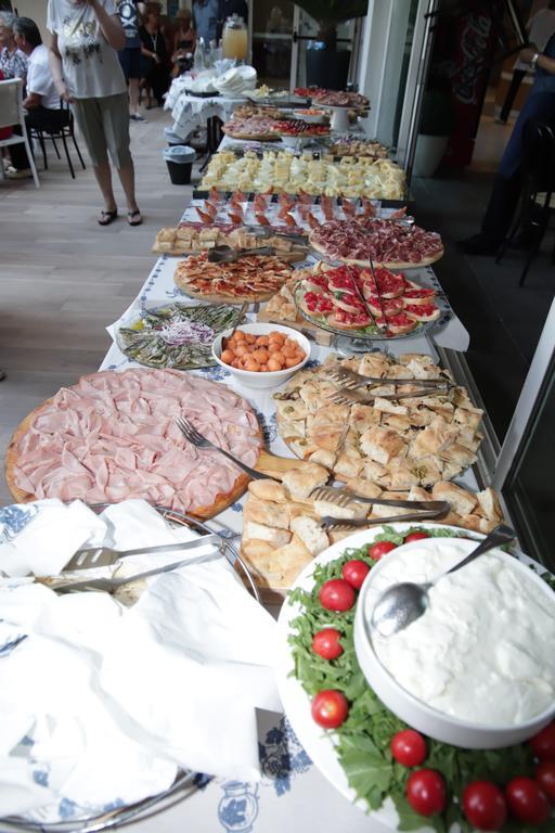 Bufetový stůl s různými druhy potravin včetně šunky, zeleniny a sýrových pokrmů.