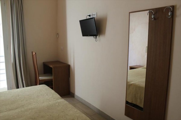 Hotelový pokoj s postelí, židlí u stolu, zrcadlem a televizí na zdi.  