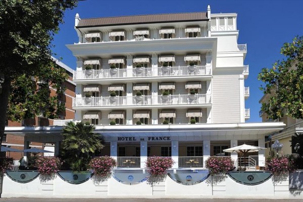 Bílo-modrý hotel s balkony, květinami a nápisem 