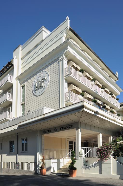 Světlý moderní hotel se zdobenými balkony a květinovou výzdobou.  