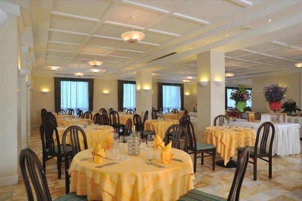 Restaurace s kulatými stoly, žlutými ubrusy a dřevěnými židlemi.