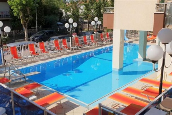 Bazén obklopený červenými lehátky a lampami na terase hotelu.