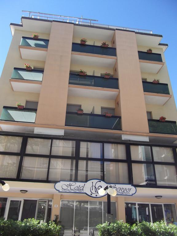 Čelní pohled na několikapatrovou budovu hotelu s balkony a květinami.