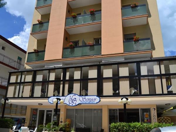 Budova hotelu s několika balkony a květinami ve žluté fasádě.