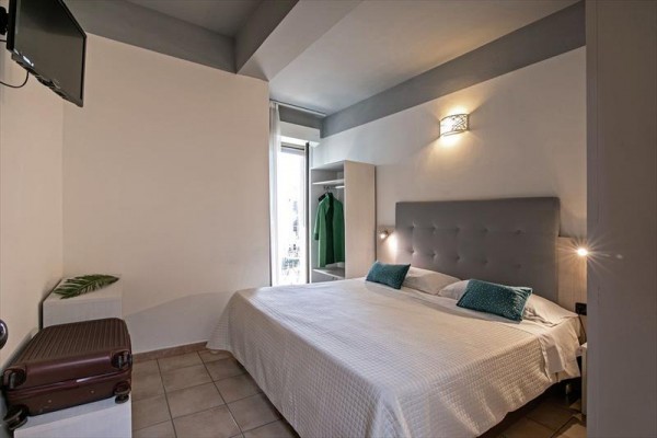 Moderní ložnice s manželskou postelí, otevřeným šatníkem a kufrem vedle.