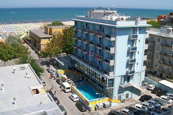Modrý hotel s bazénem poblíž pláže a moře.