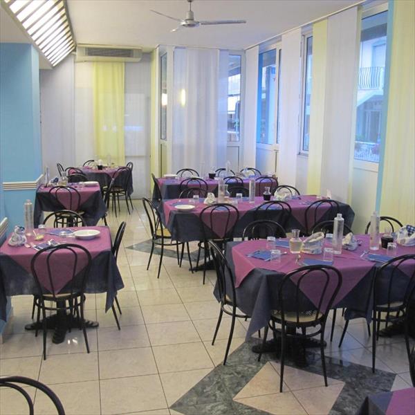 Restaurace se stoly pokrytými fialovými ubrusy a černými židlemi.