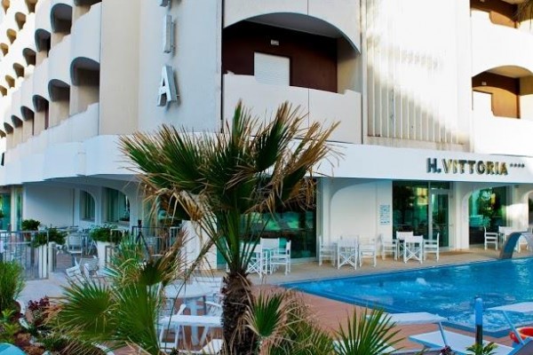 Moderní hotel se skleněným oplocením a malým bazénem před vchodem.