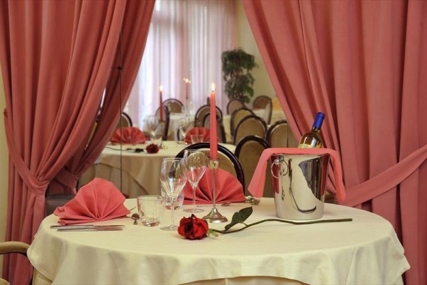 Elegantně prostřený stůl s růží, svíčkou a šampaňským v kbelíku, obklopený růžovými závěsy.