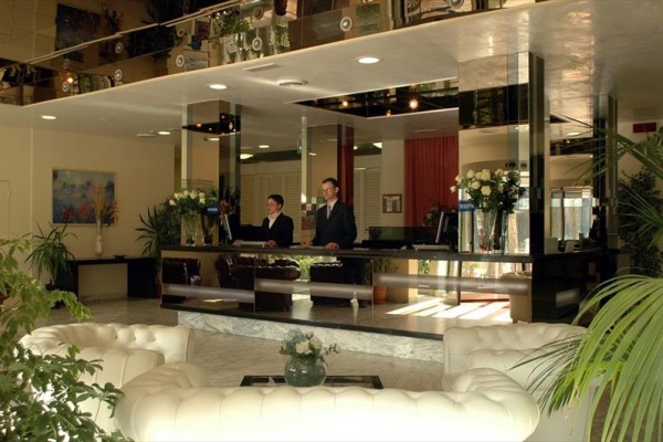 Recepce hotelu s dvěma zaměstnanci v elegantním prostředí plném zeleně a květin.